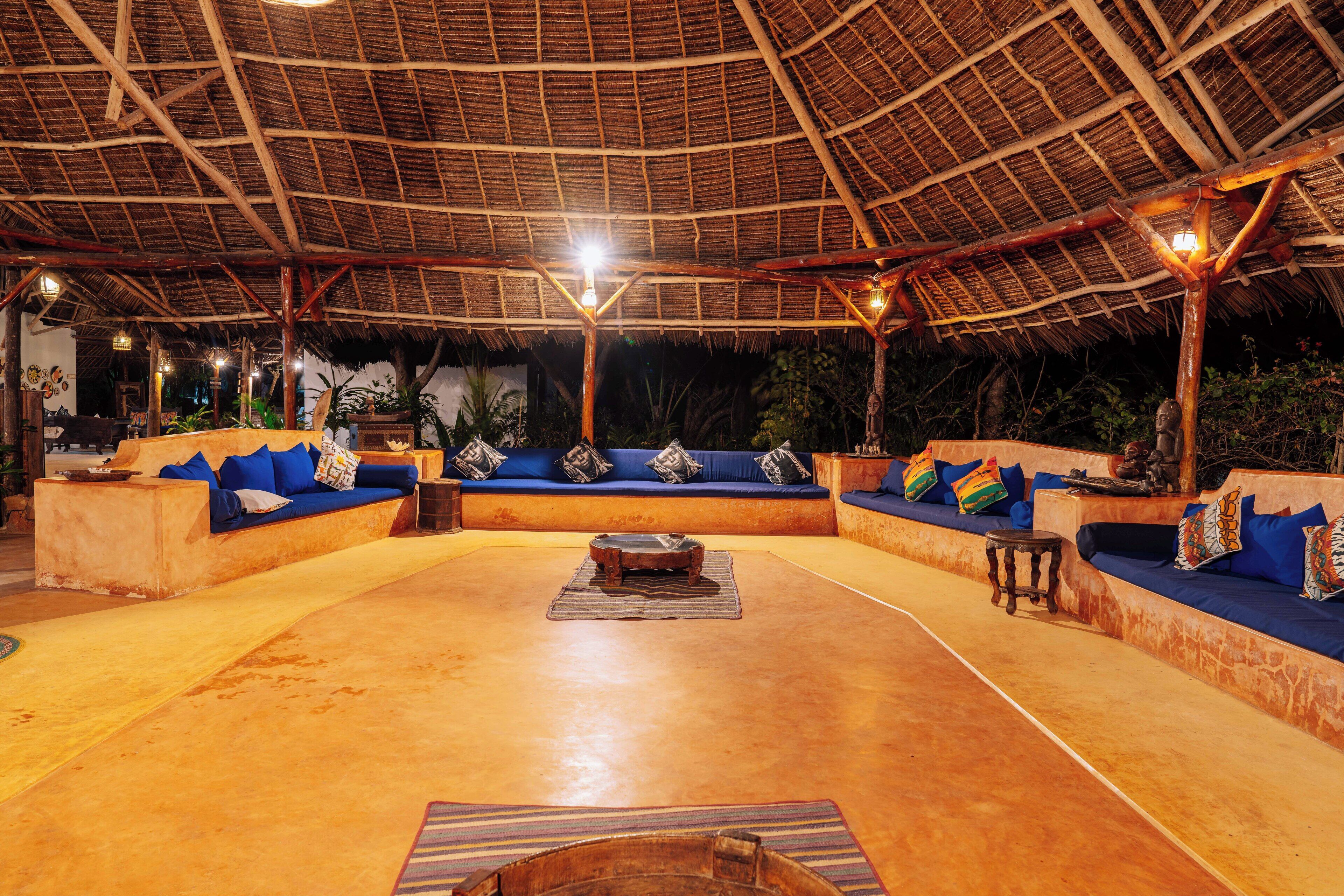 An open-plan lounge area with a thatched roof, cushioned seating, and a central coffee table.