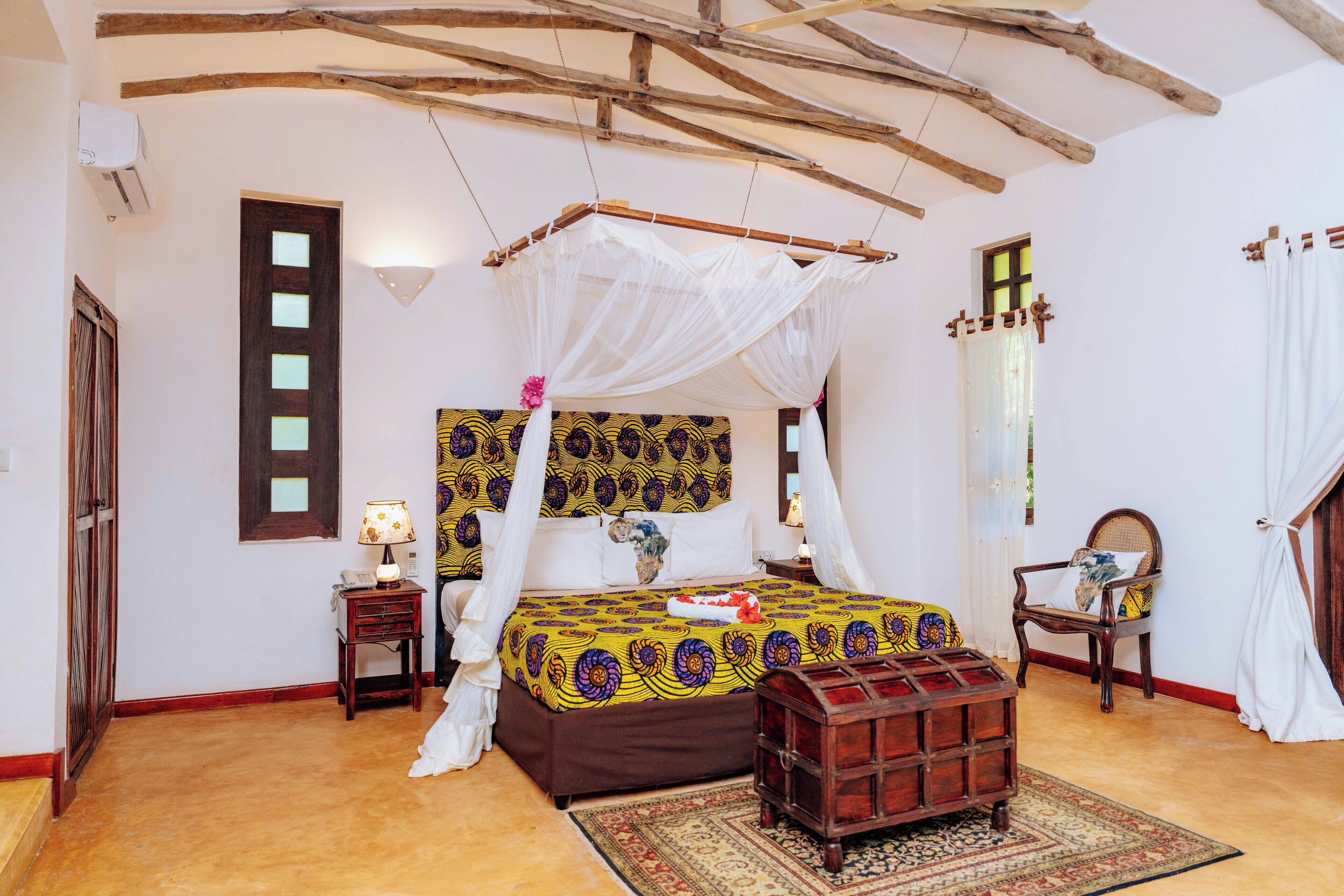 A room with a bed, a nightstand, a chair, a wooden chest, and a large window.