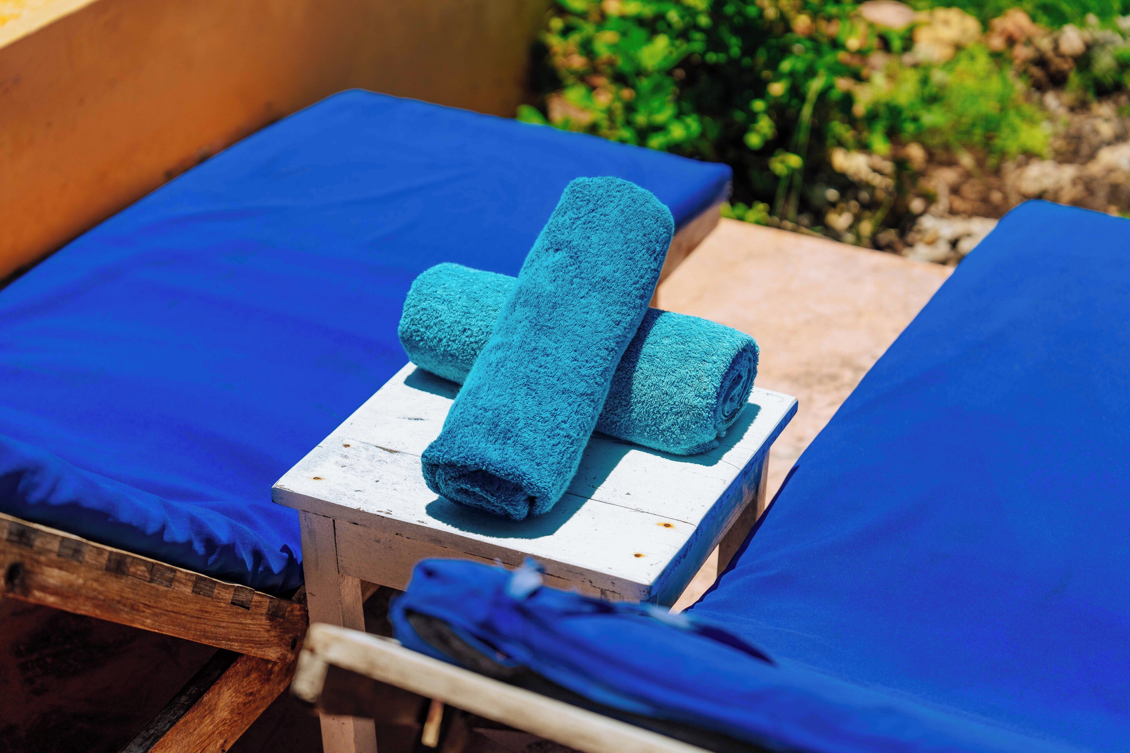 A wooden chair with a blue towel and a rolled towel on top.