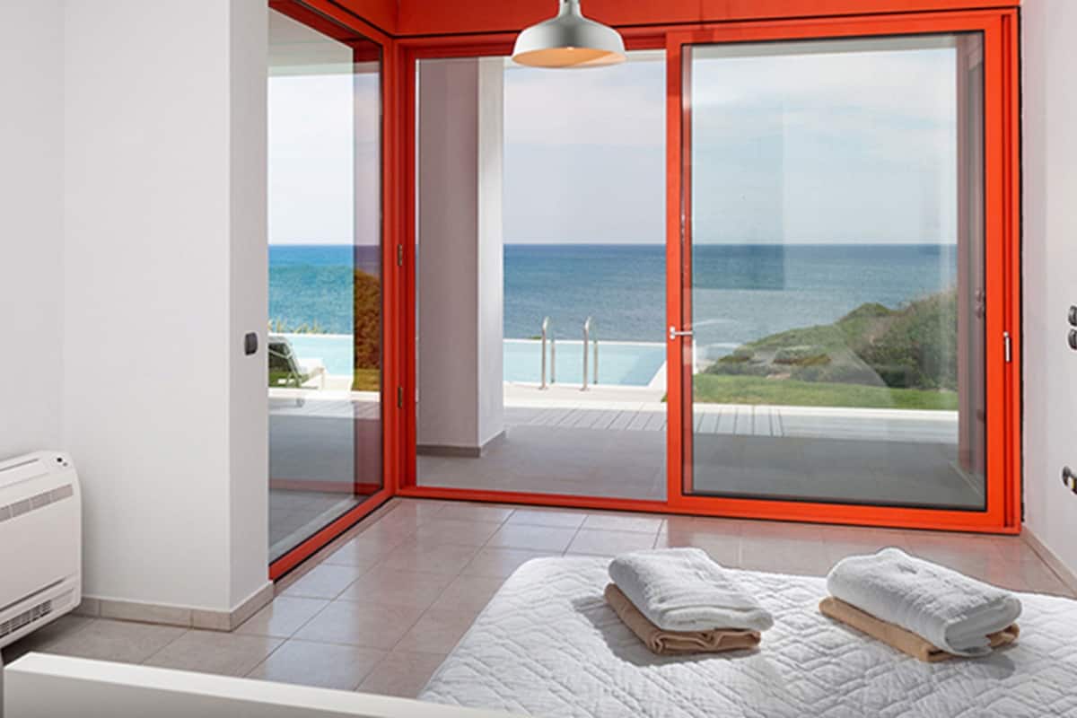 A modern bedroom with a large sliding glass door leading to a balcony with a view of the sea.