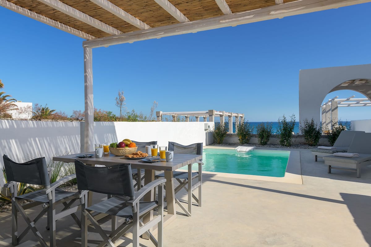 An outdoor patio with a pool, white walls, and a view of the sea.