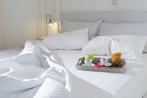 A neatly made bed with white linens, a tray with a green apple, a cup of coffee, and a pastry. - White Village (Rhodes)