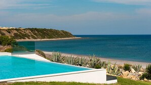 A modern pool with a clear view of the ocean and a rocky hillside in the background. - White Village (Rhodes)