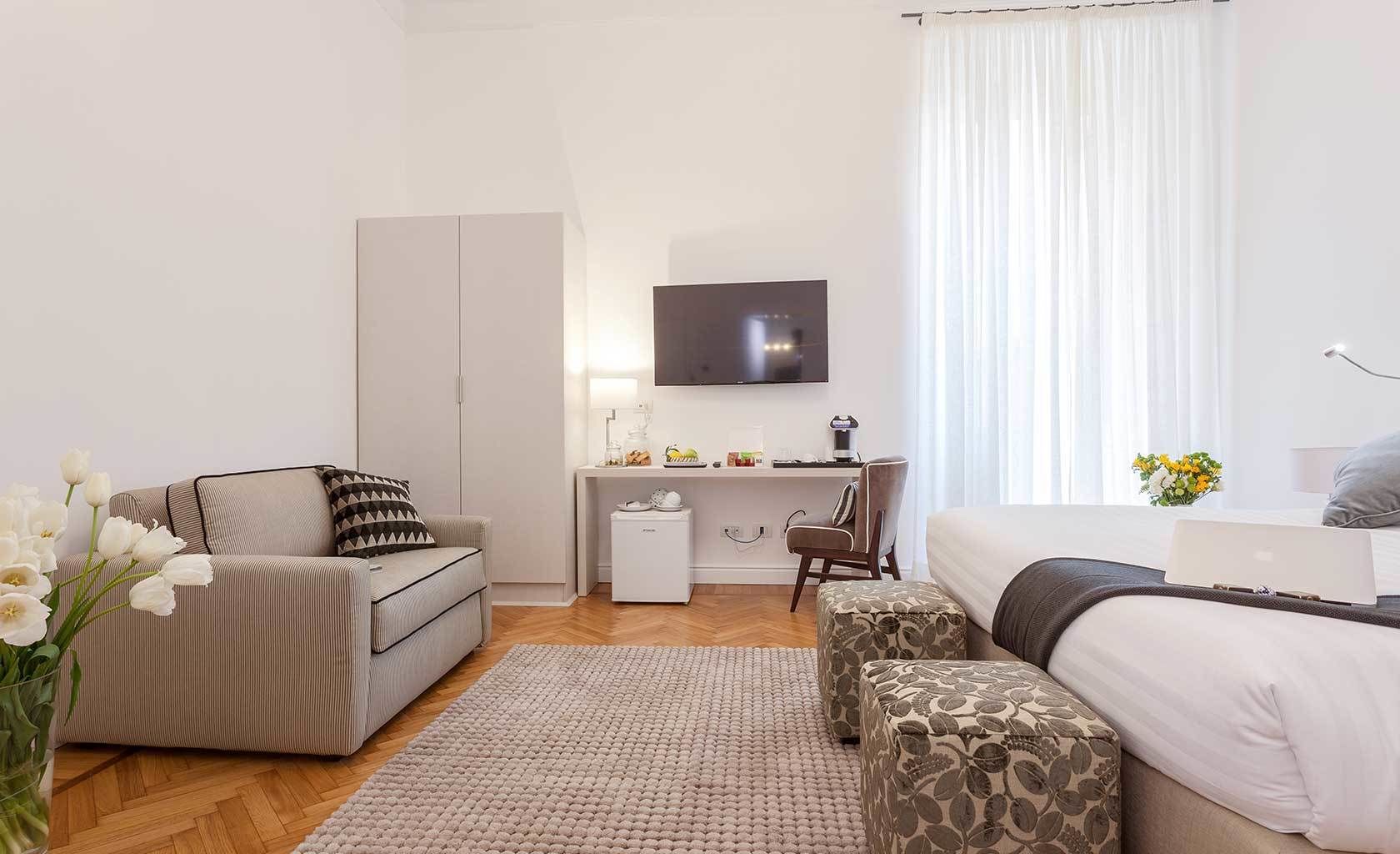 Ett modernt hotellrum med en soffa, ett skrivbord med en dator, en säng och en TV.