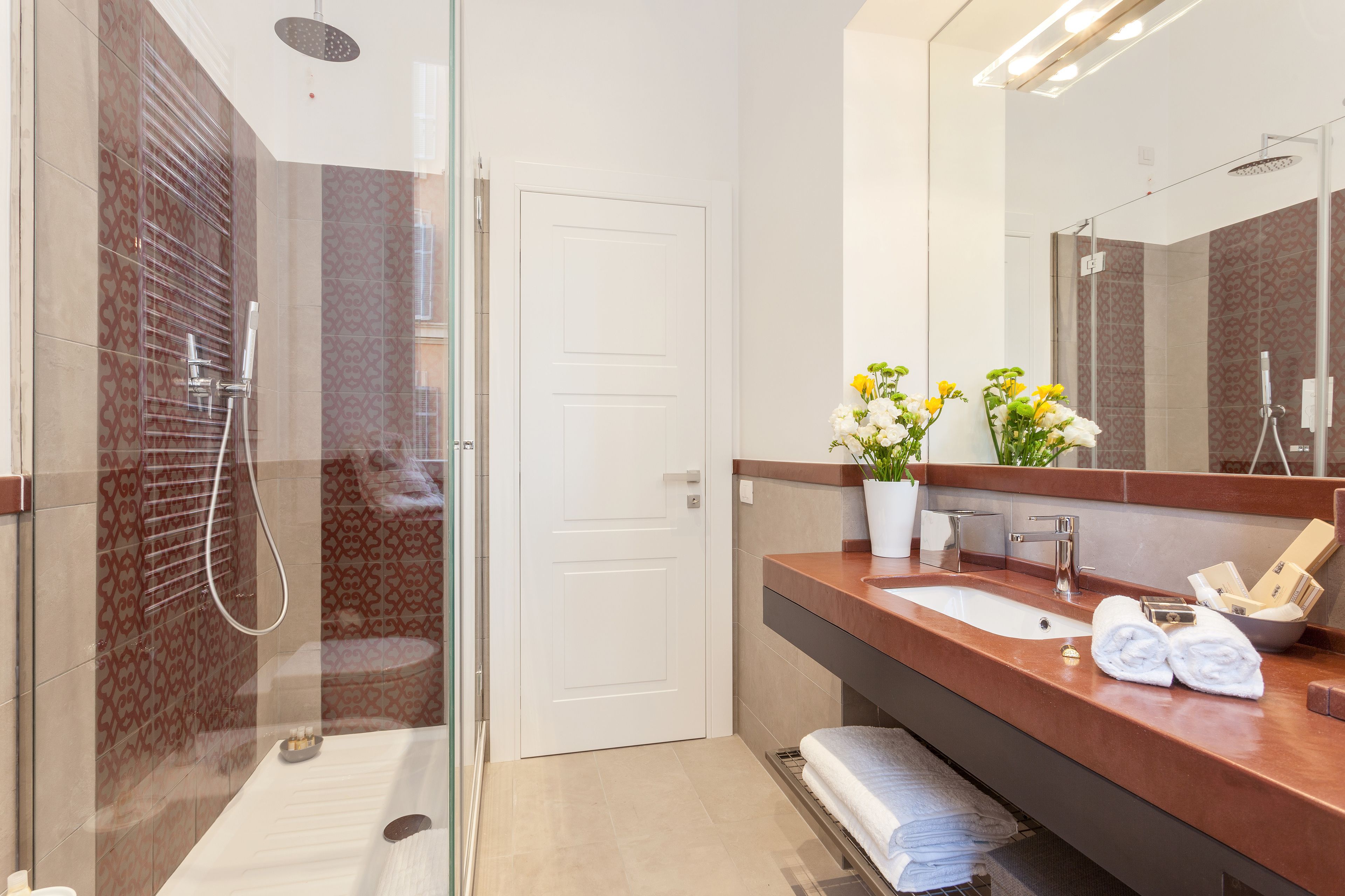 A modern bathroom with a glass-enclosed shower, a large mirror, and a wooden vanity with a sink and towel rack.