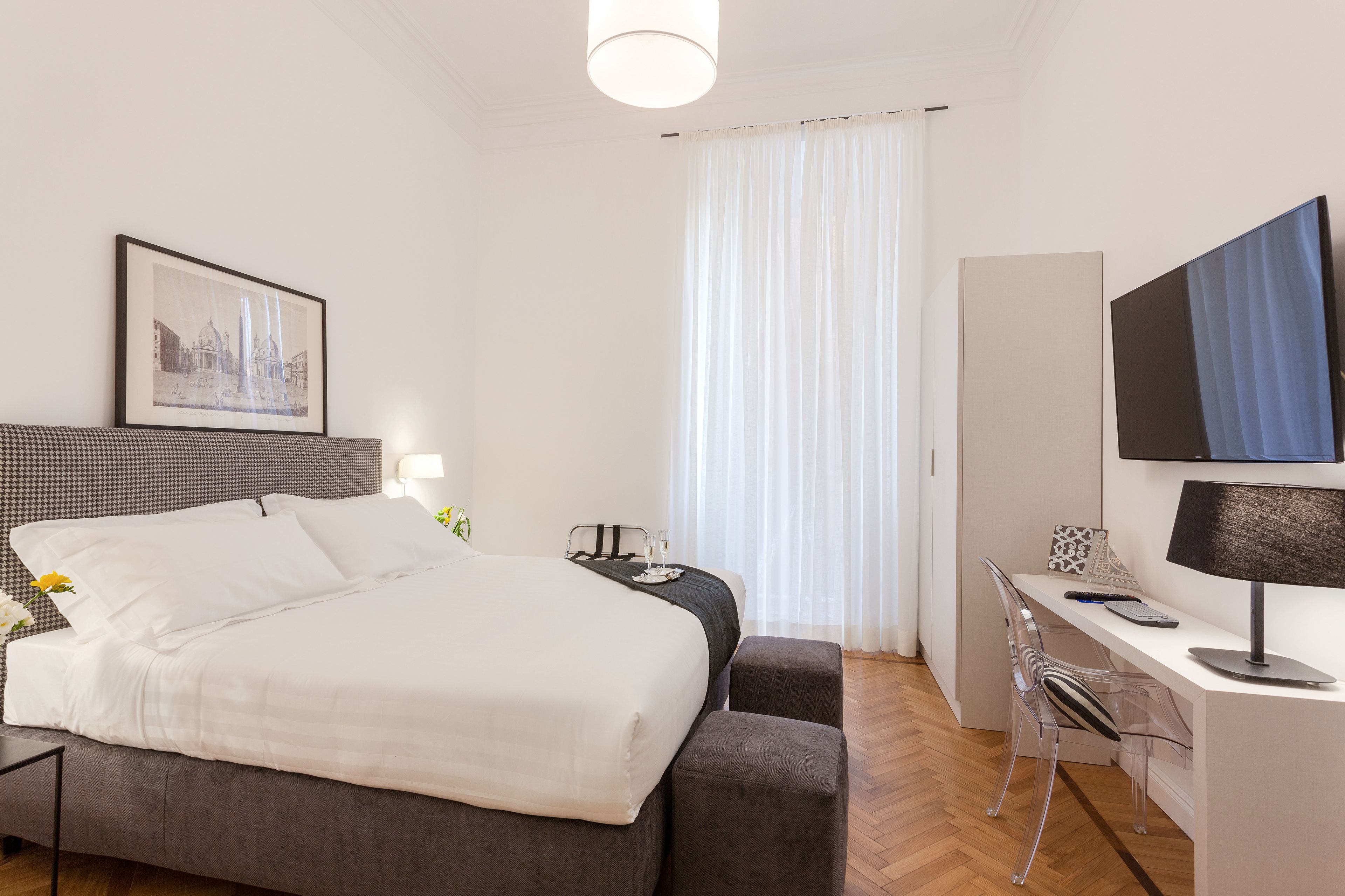 Une chambre d’hôtel avec un lit, un bureau, une chaise, une télévision et une fenêtre avec des rideaux.