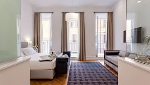 A modern hotel room with a bed, a desk, a sofa, and a large window with curtains. - 504 Corso Suites (Rome)