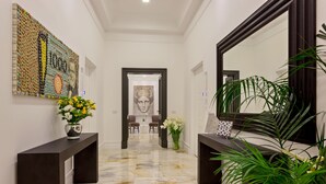 A hallway with a marble floor, a large mirror, and a wall art piece made of bottles. There are two dark wooden consoles with vases of flowers. - 504 Corso Suites (Rome)