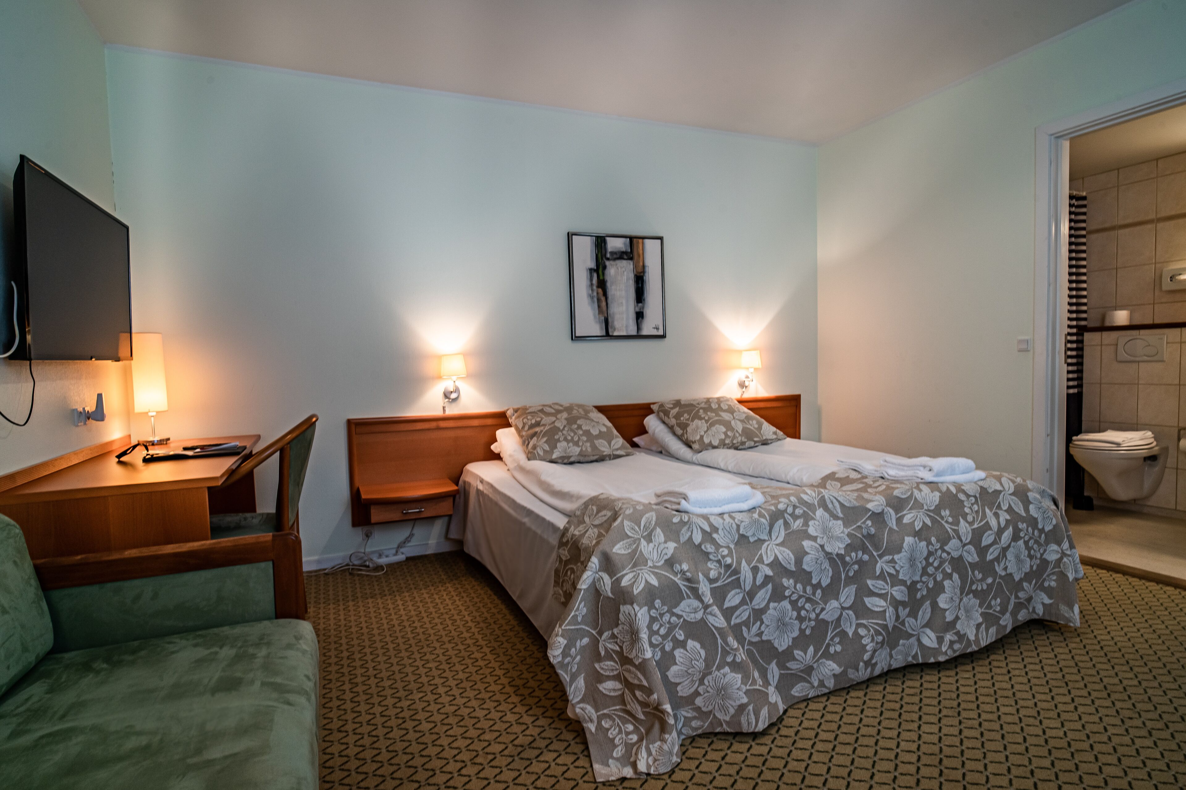 A hotel room with a bed, two bedside lamps, a flat-screen TV, a desk, and a chair.