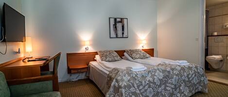 A hotel room with a bed, two bedside lamps, a flat-screen TV, a desk, and a chair.