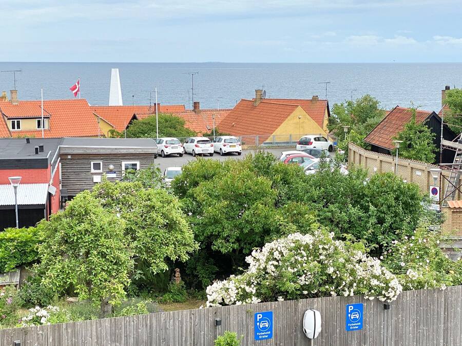 A coastal town with red-roofed buildings, a parking sign, and a view of the sea.