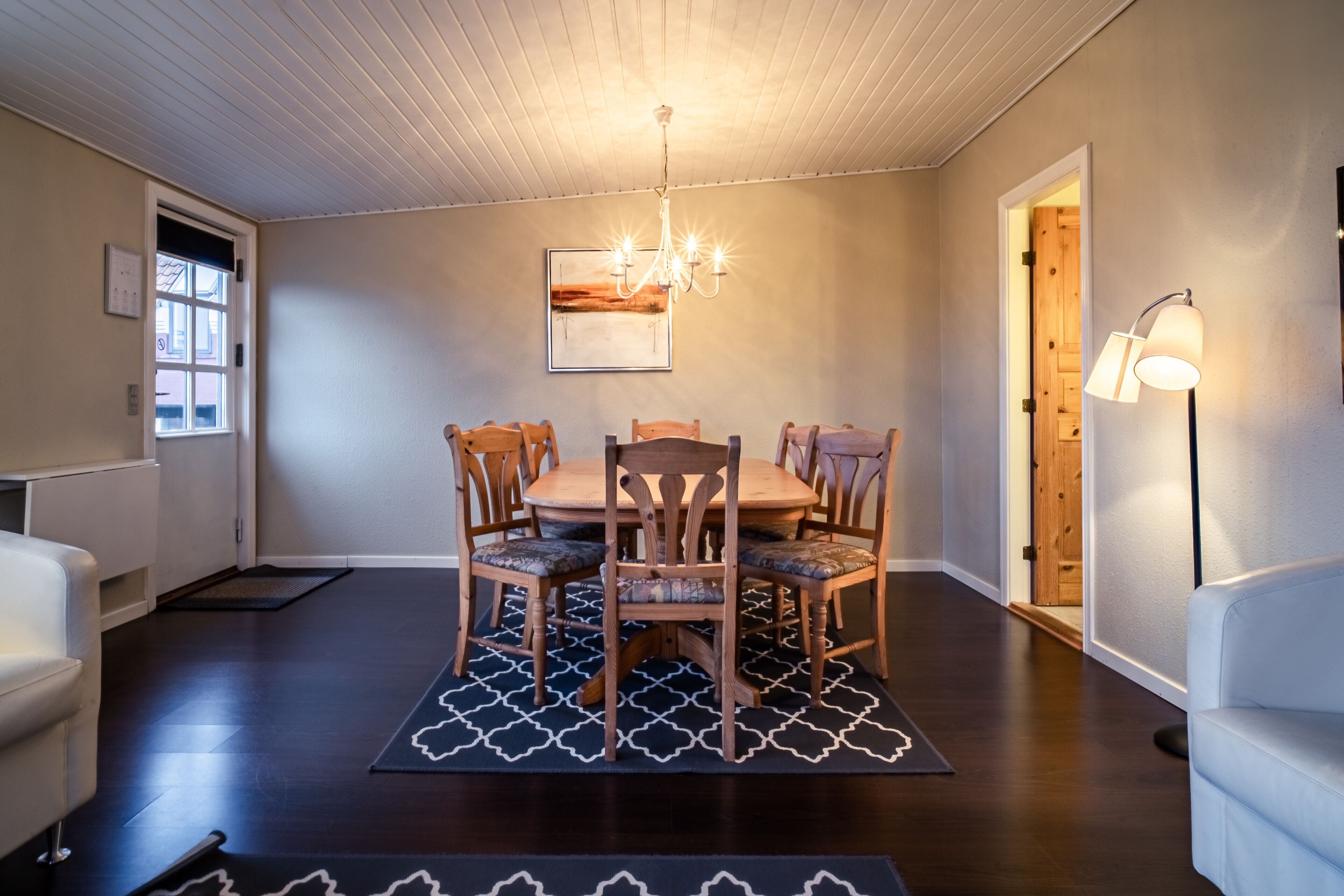 A dining area with a wooden table and chairs, a chandelier, and a patterned rug.