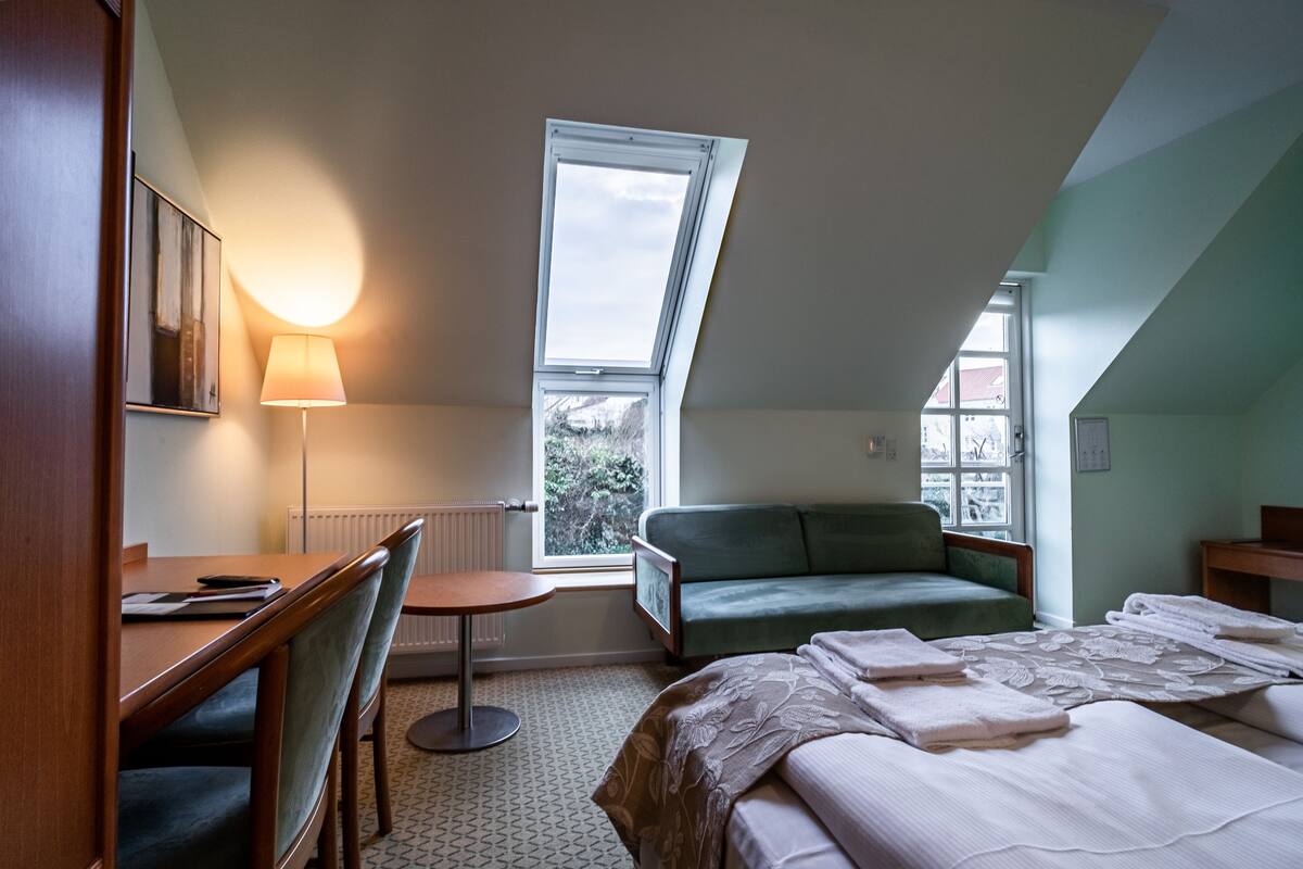 A hotel room with a bed, a desk, a chair, a small table, and a couch.