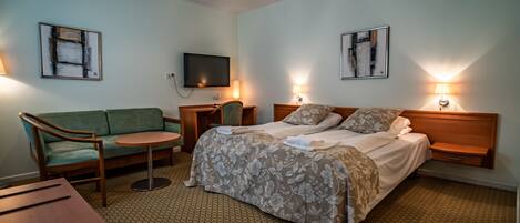 A hotel room with a bed, a sofa, a small table, and a TV on the wall.