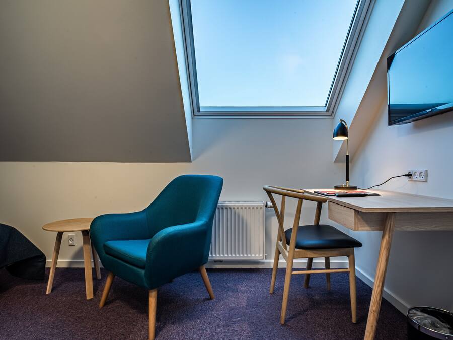 A room with a skylight, a desk, two chairs, a radiator, and a TV mounted on the wall.