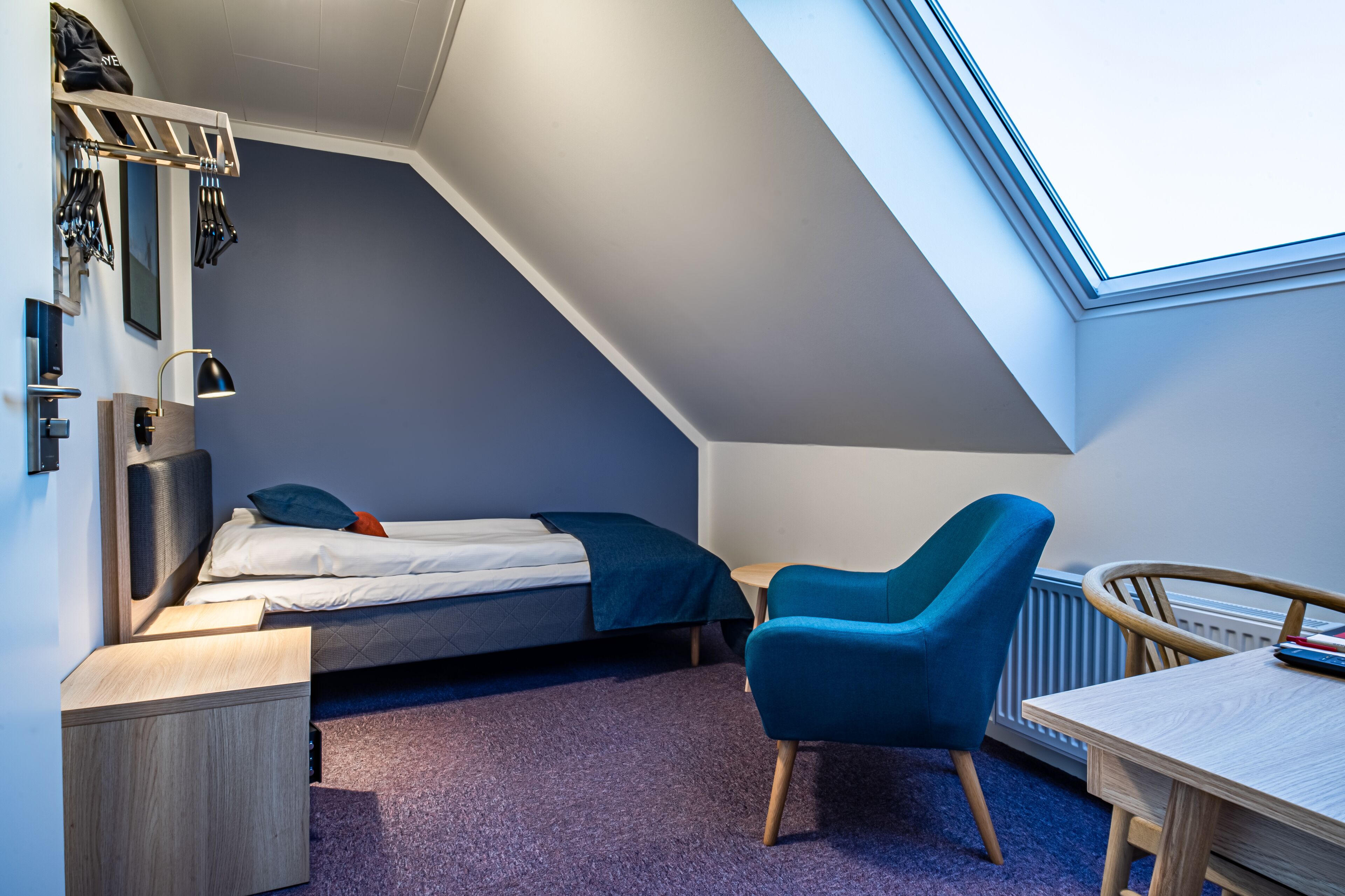 Ein gemütliches Schlafzimmer mit Bett, Schreibtisch, Stuhl und Dachfenster.