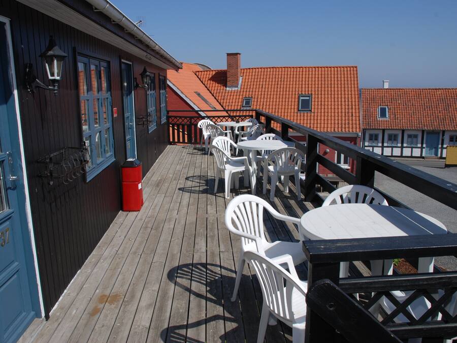 A wooden deck with white plastic chairs and tables, a red trash bin, and a blue door with the number 37.