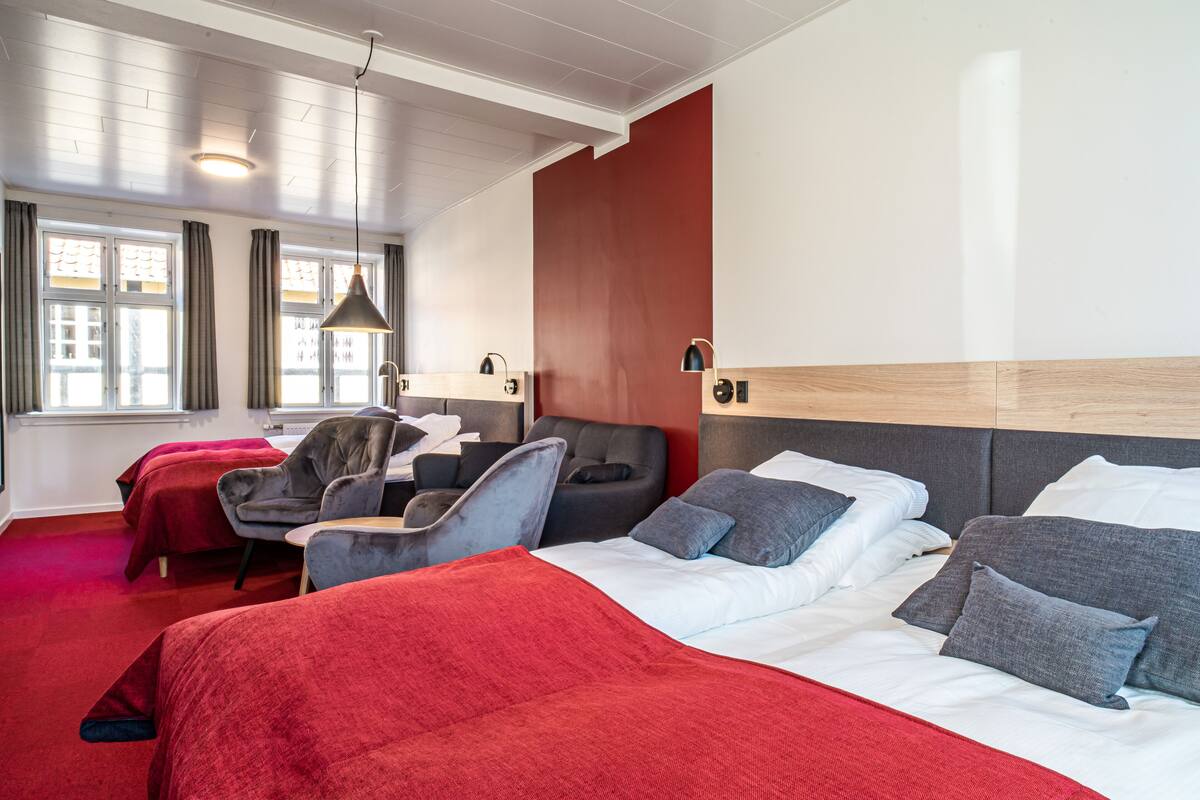 A hotel room with two beds, a red carpet, a large window with curtains, and a modern light fixture.