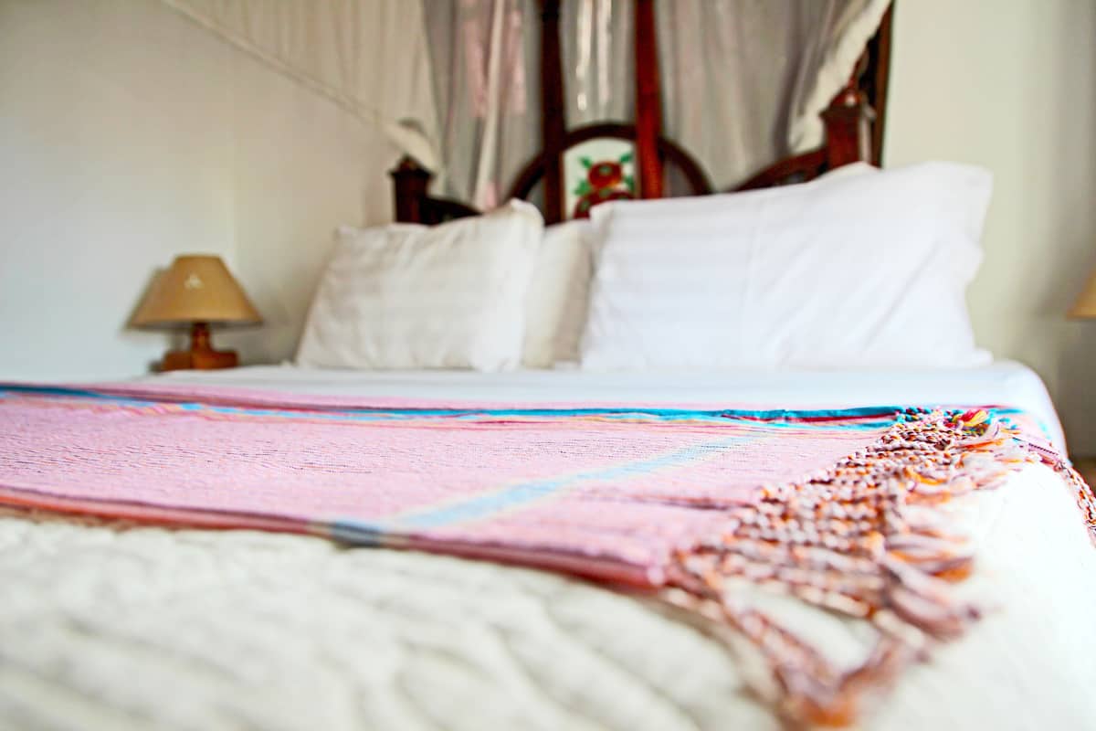 A bed with a colorful blanket and white pillows, a wooden headboard, and a bedside lamp.