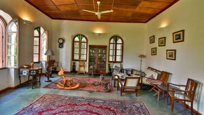 A spacious room with a high ceiling, wooden beams, and a large, ornate rug. There are several wooden chairs and a sofa arranged around a central area with a small table. - Hiliki House (Zanzibar Town)