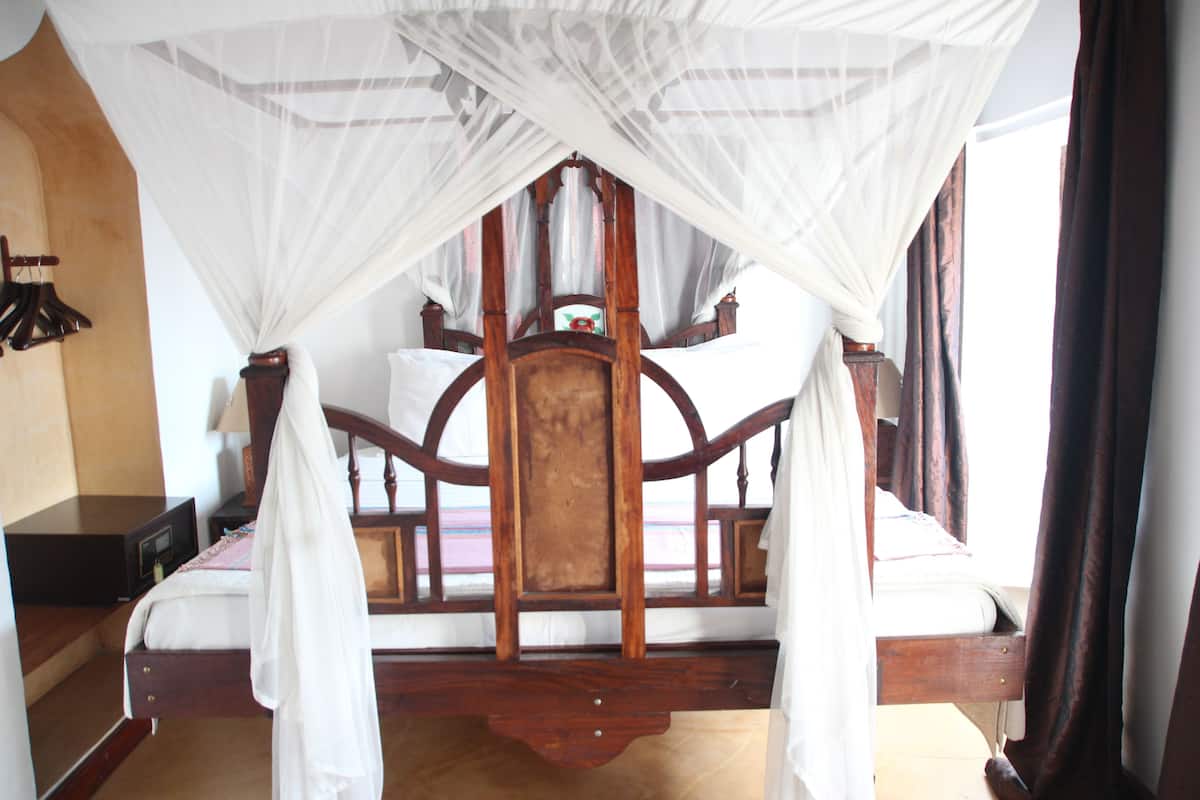 A four-poster bed with a canopy, wooden headboard, and a nightstand with a lamp.