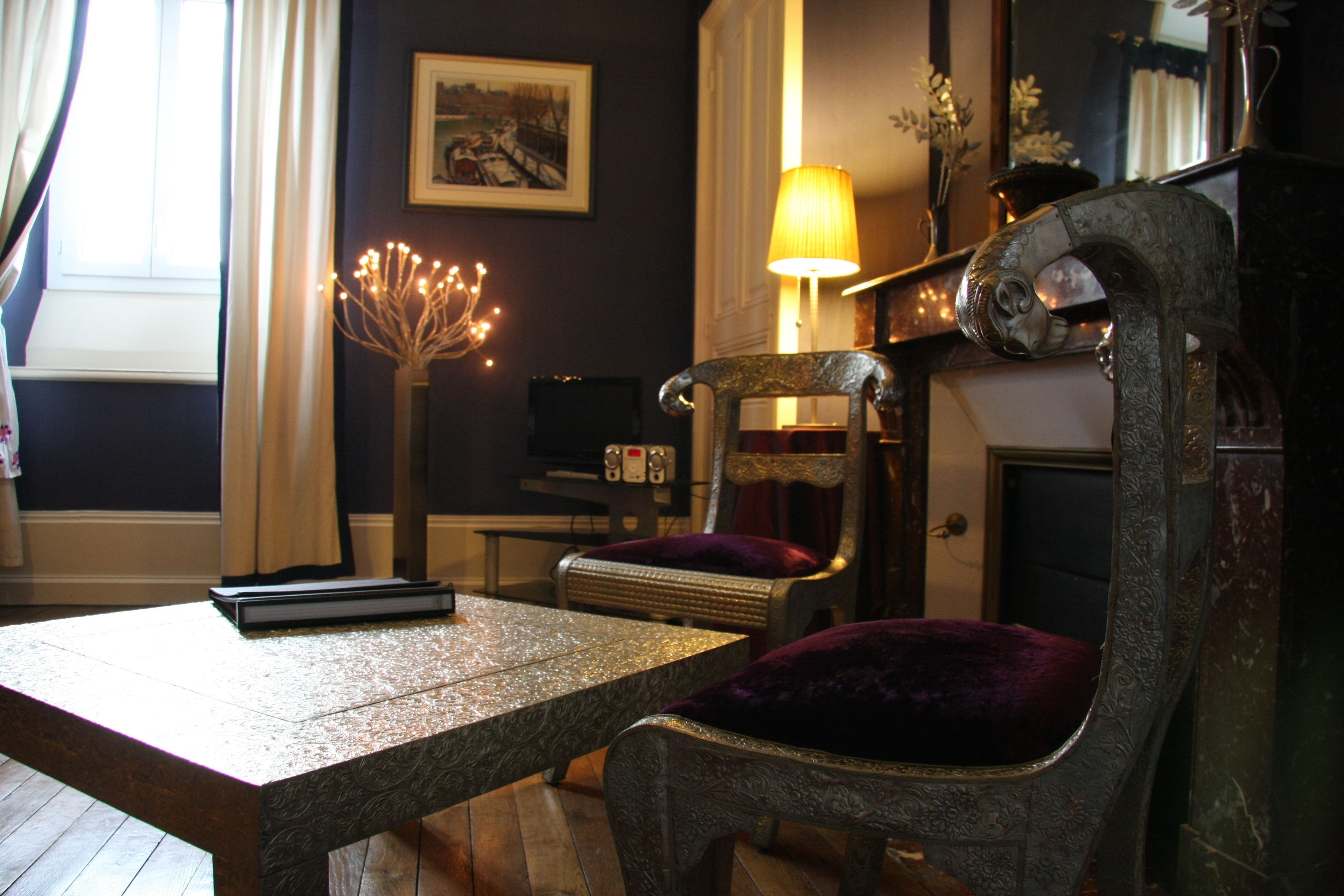 A room with a wooden table, two upholstered chairs, a lamp, and a fireplace.