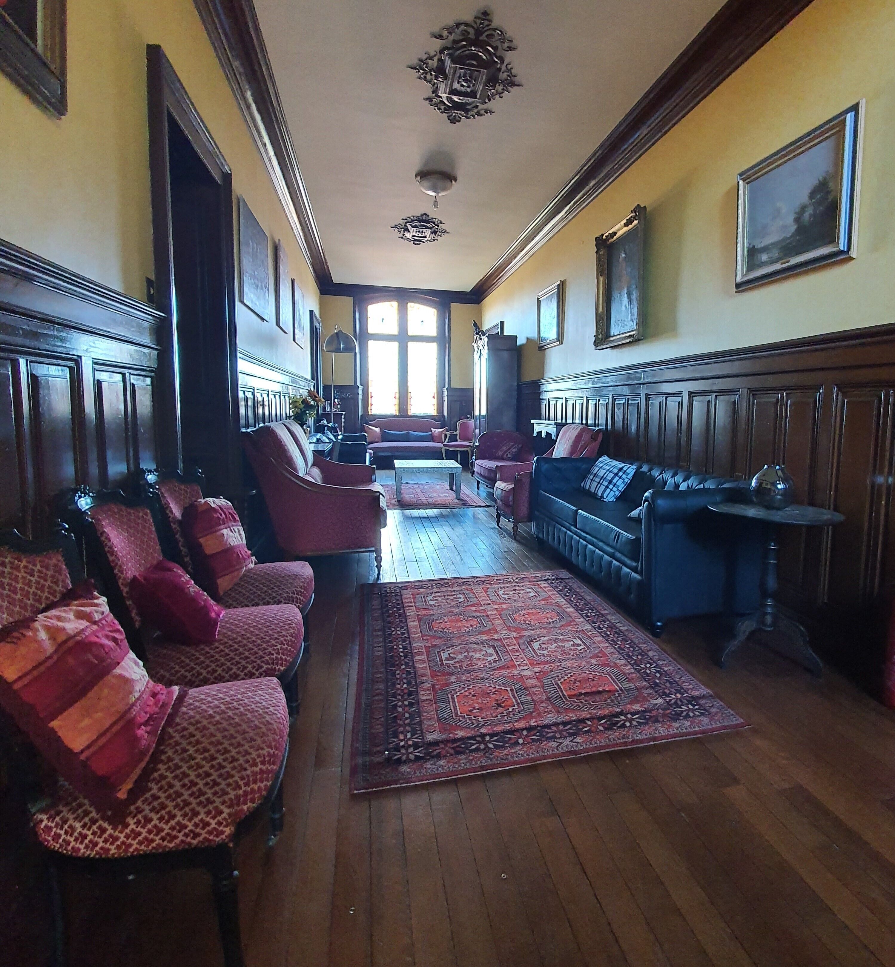 A long, narrow room with wooden floors, a patterned rug, and rows of upholstered chairs and sofas.