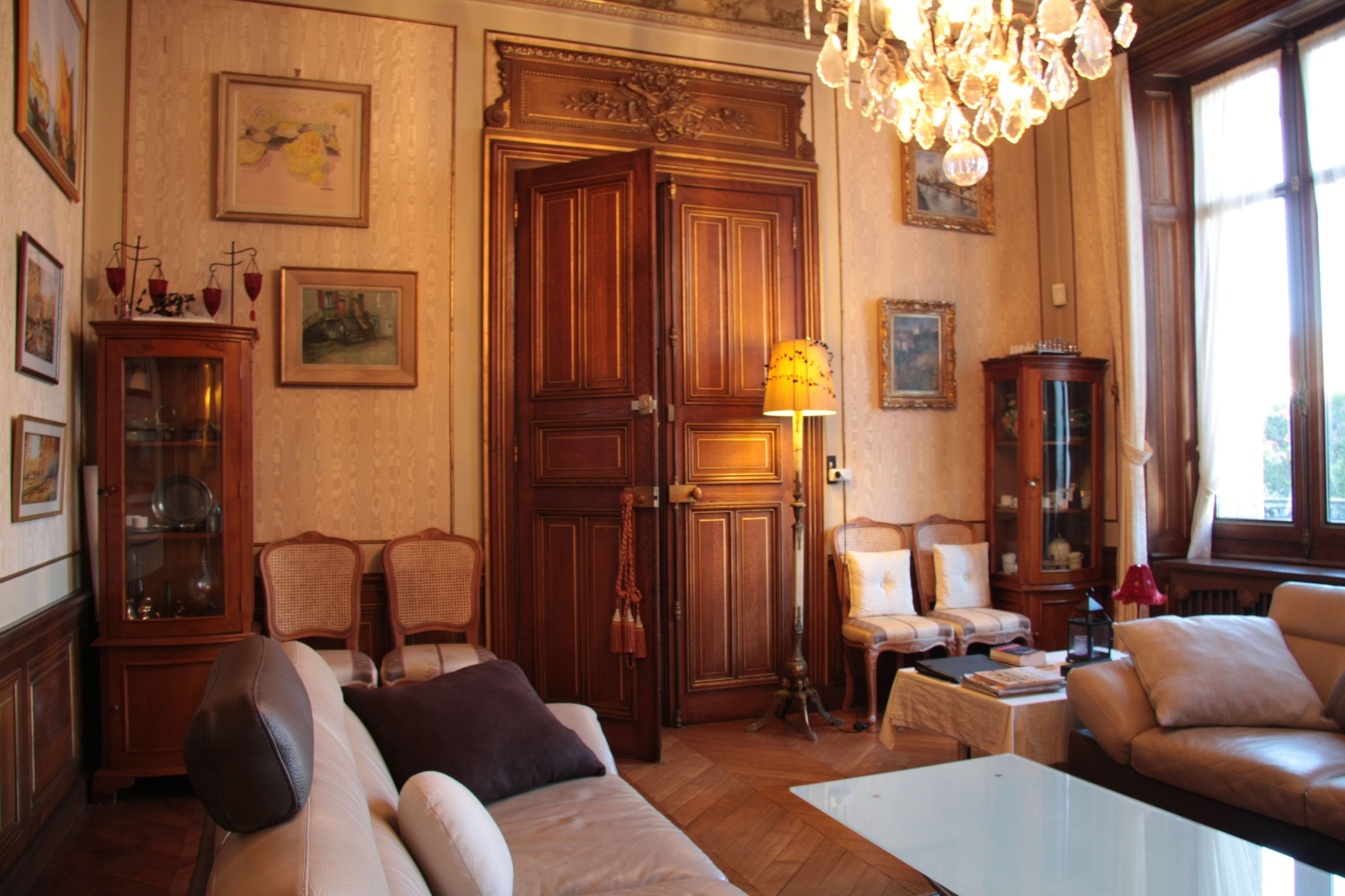 Une pièce au décor traditionnel, avec une grande armoire en bois, une vitrine, deux canapés, une table et un lustre.