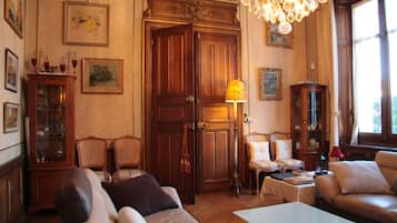Une pièce au décor traditionnel, avec une grande armoire en bois, une vitrine, deux canapés, une table et un lustre.