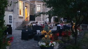 An outdoor seating area with tables and chairs, surrounded by potted plants and flowers. - Villa Primerose (Arcis-sur-Aube)