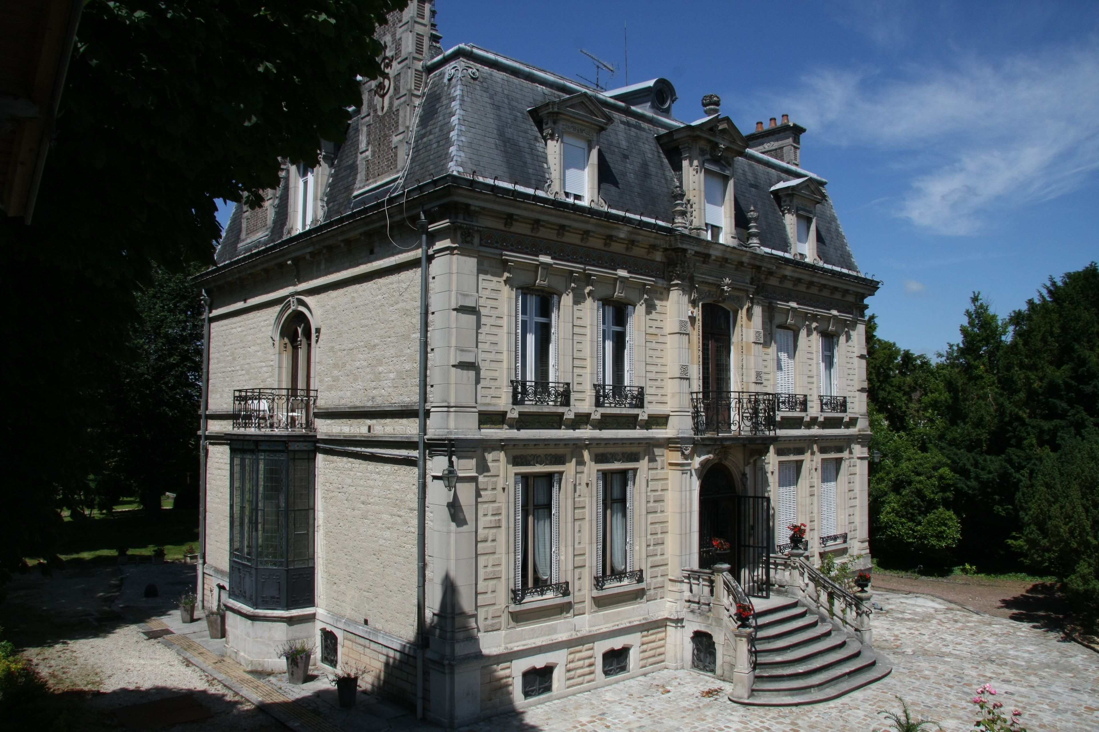 Ein historisches Gebäude mit einer symmetrischen Fassade, großen Fenstern und einem zentralen Eingang mit einer Treppe.