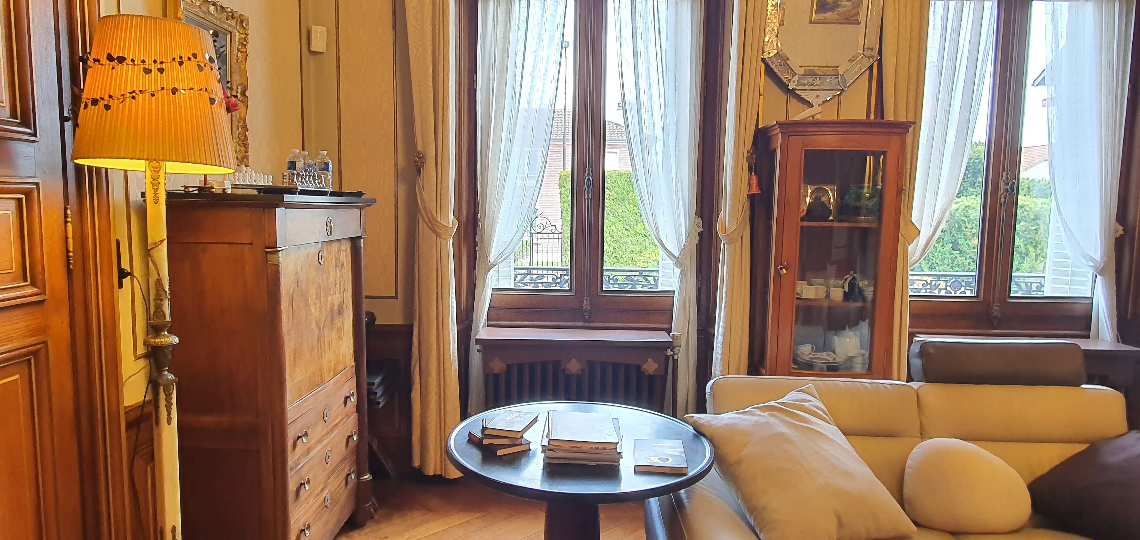 A cozy room with a wooden cabinet, a table with books, a sofa, and a window with curtains.