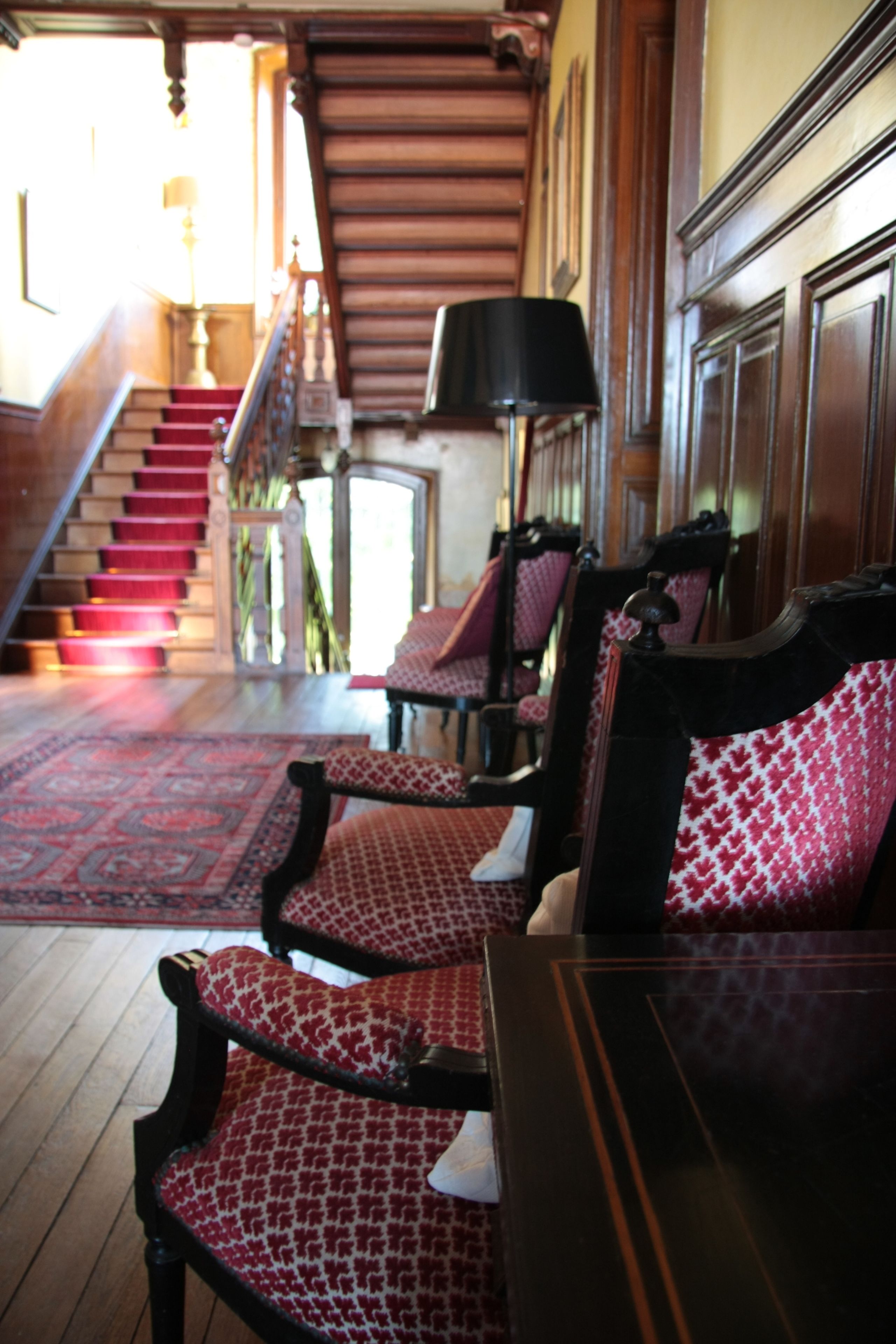 A lobby with a staircase, red carpeted stairs, and patterned chairs.