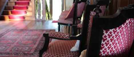 A lobby with a staircase, red carpeted stairs, and patterned chairs.