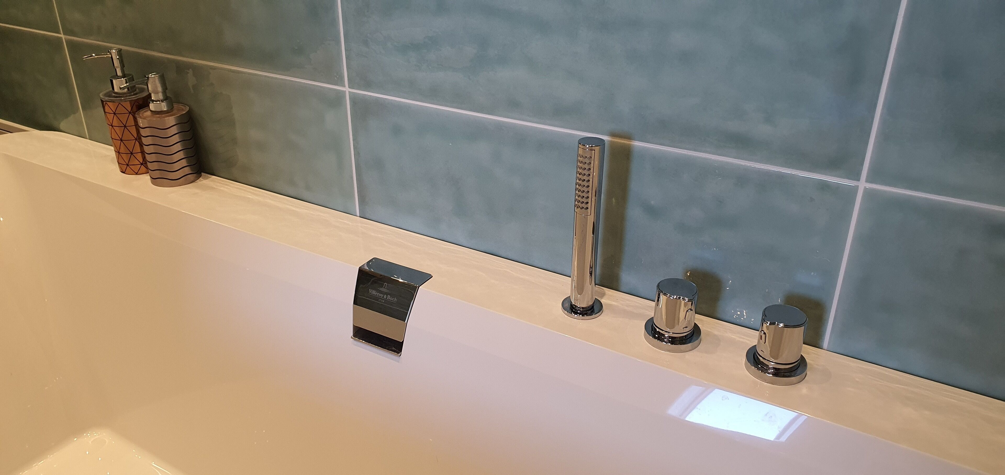 A bathroom with a bathtub, a handheld showerhead, and two bottle-shaped soap dispensers.