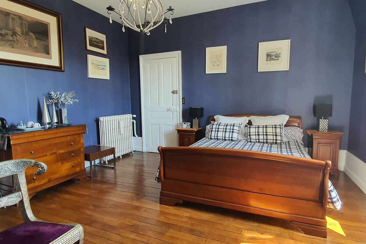 Quarto com cama de madeira, cómoda, cadeira e radiador.