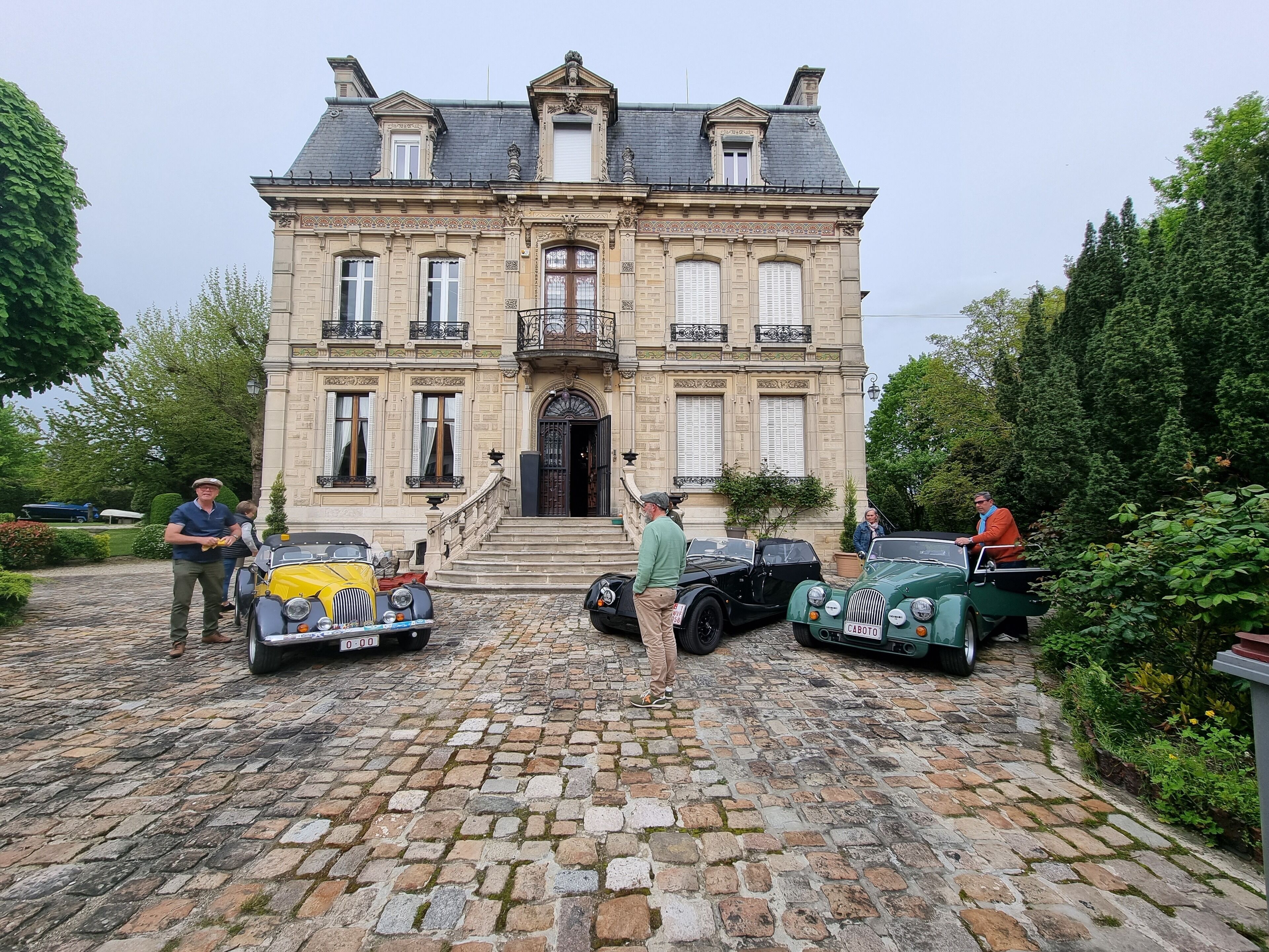A historic building with a cobblestone driveway and classic cars parked in front.