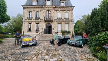 A historic building with a cobblestone driveway and classic cars parked in front.