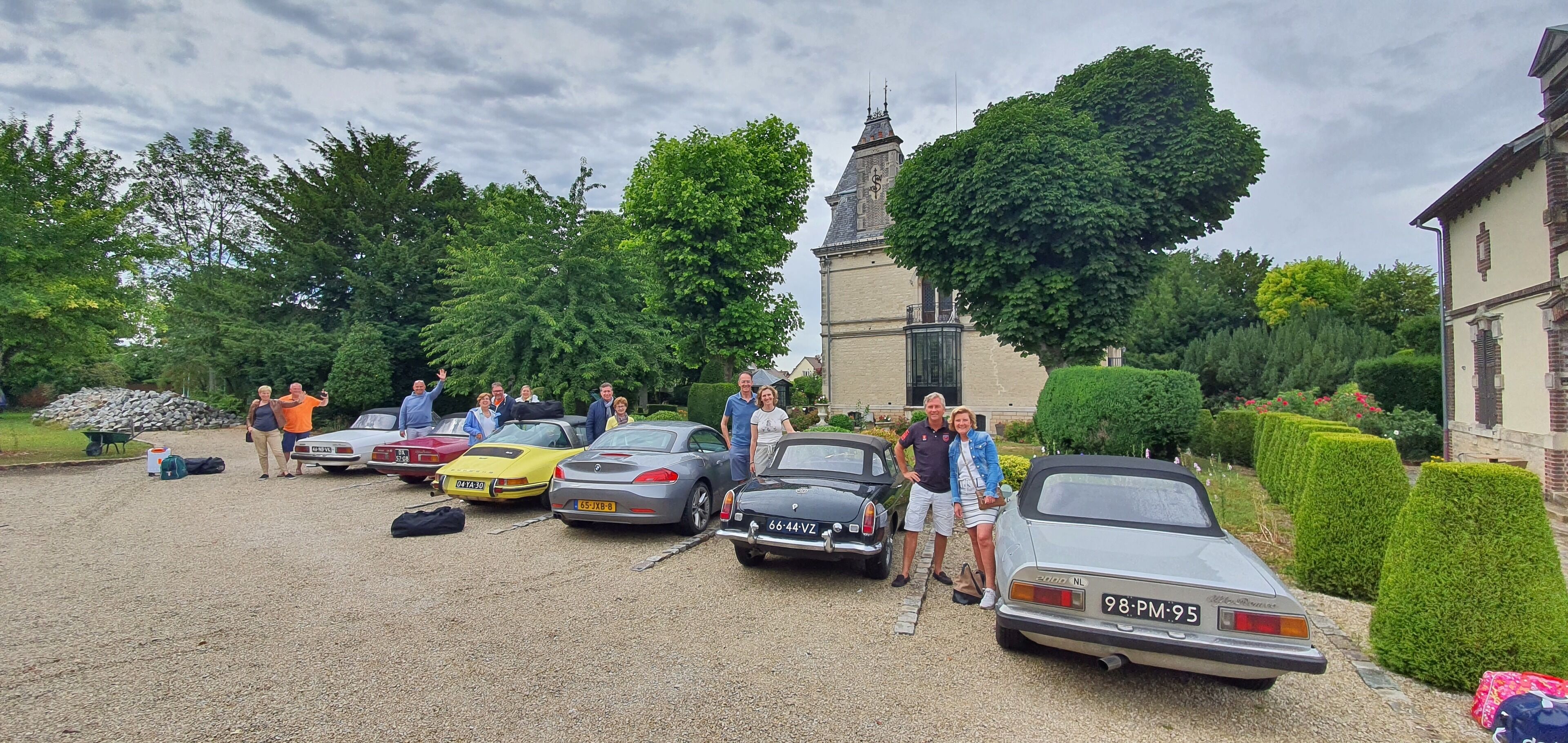 Un groupe de voitures anciennes est garé dans une allée, avec un bâtiment historique en arrière-plan.