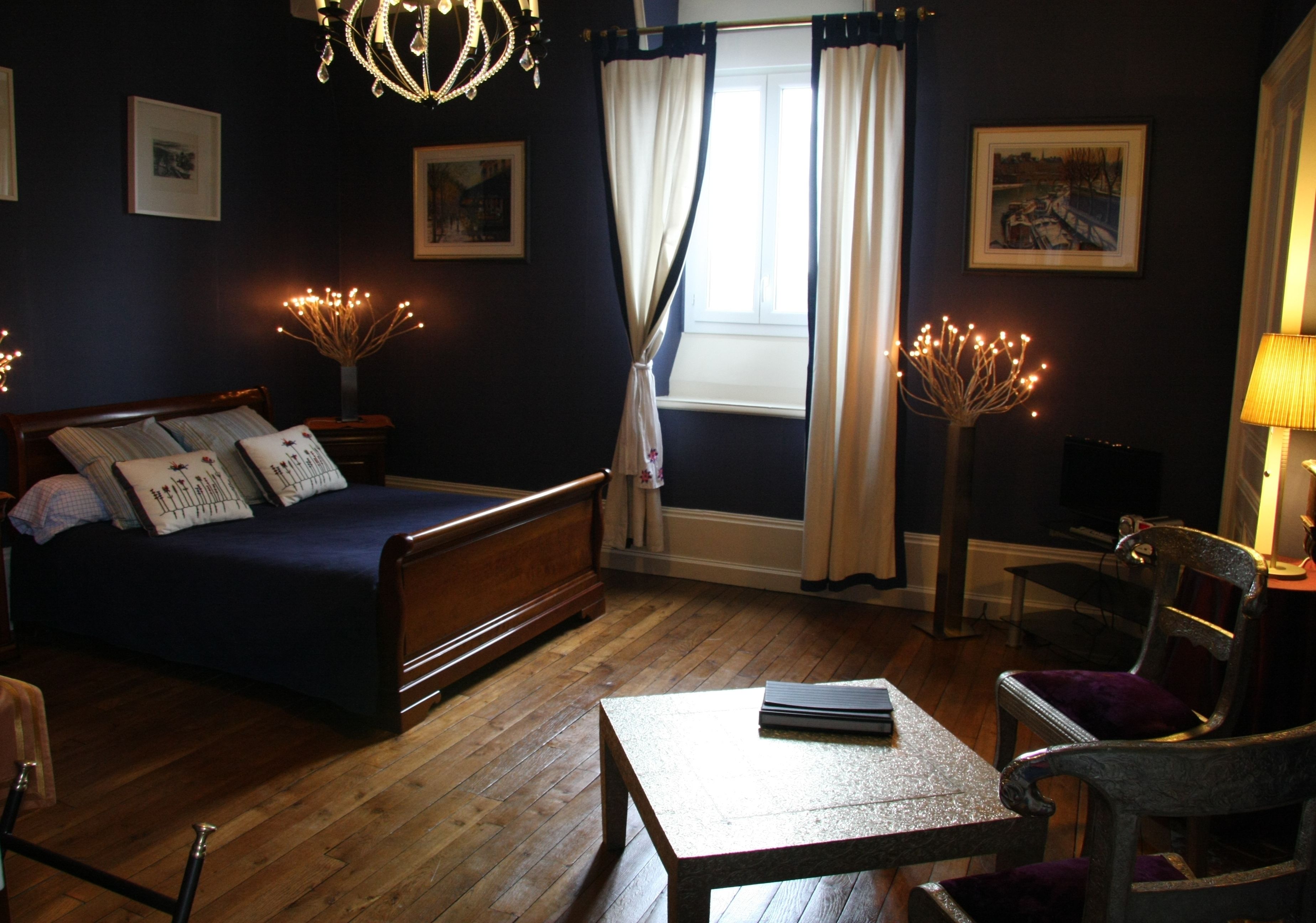 A bedroom with a bed, a small table, a chair, a lamp, and a window with curtains.