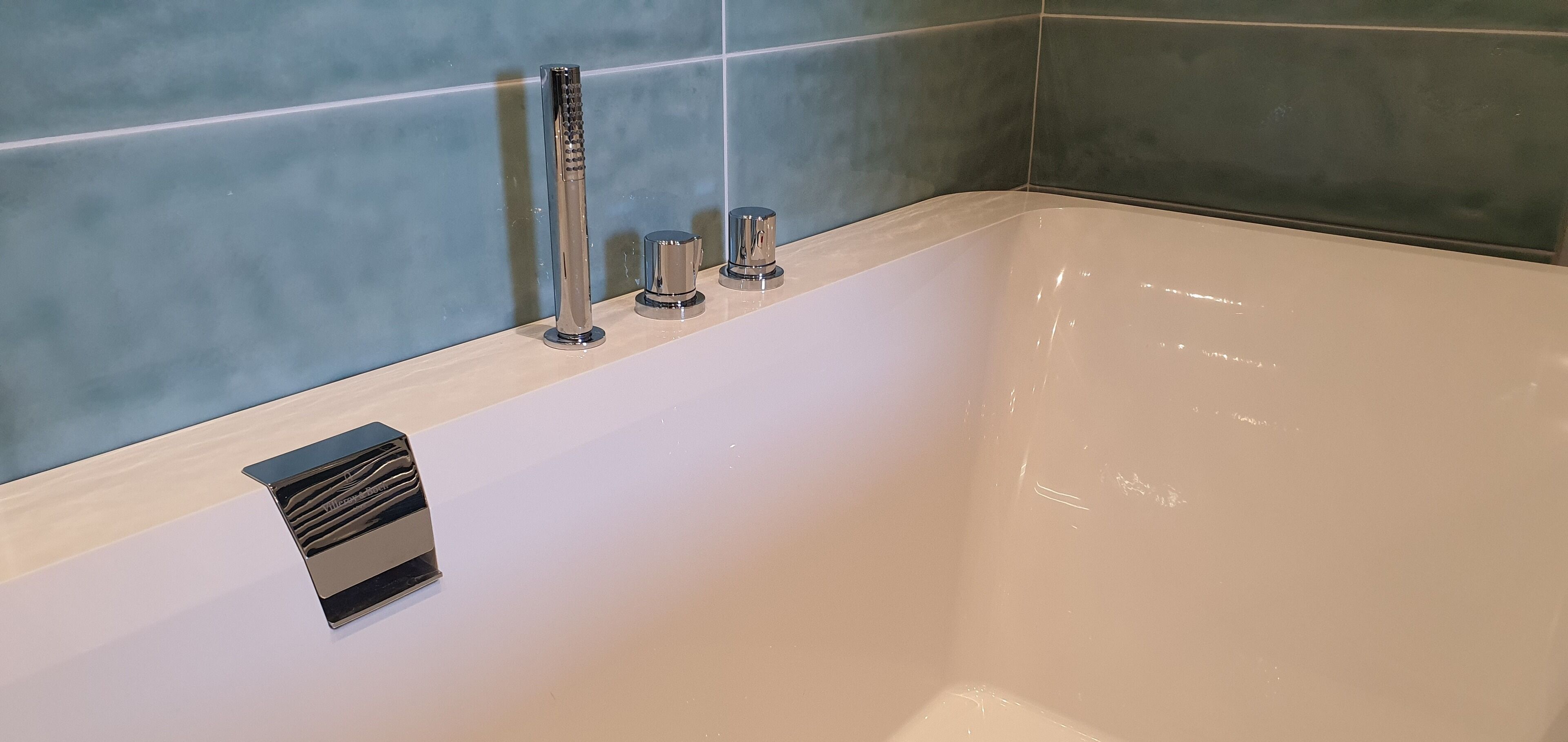 Une baignoire avec des robinets chromés et une bouche d’aération dans le mur.