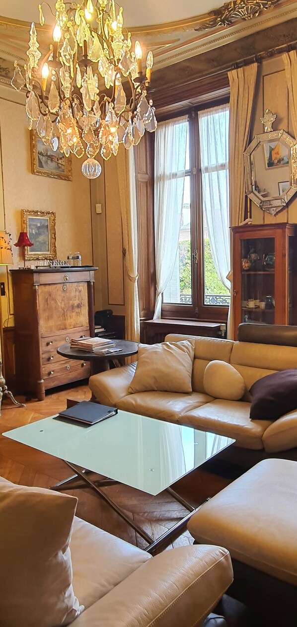 A living room with a chandelier, leather sofa, and a glass coffee table. - Villa Primerose (Arcis-sur-Aube)