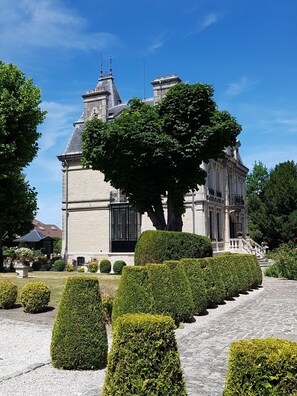 A large, historic building with a prominent tower and a well-manicured garden with neatly trimmed hedges and a central tree. - Villa Primerose (Arcis-sur-Aube)