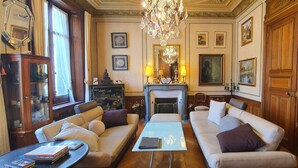 A spacious living room with a fireplace, two sofas, a coffee table, and a chandelier. - Villa Primerose (Arcis-sur-Aube)