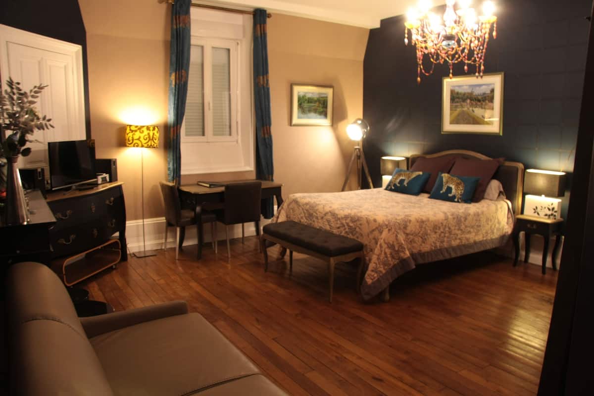 Quarto com cama, mesas de cabeceira, escrivaninha, cadeira, televisão e lustre.