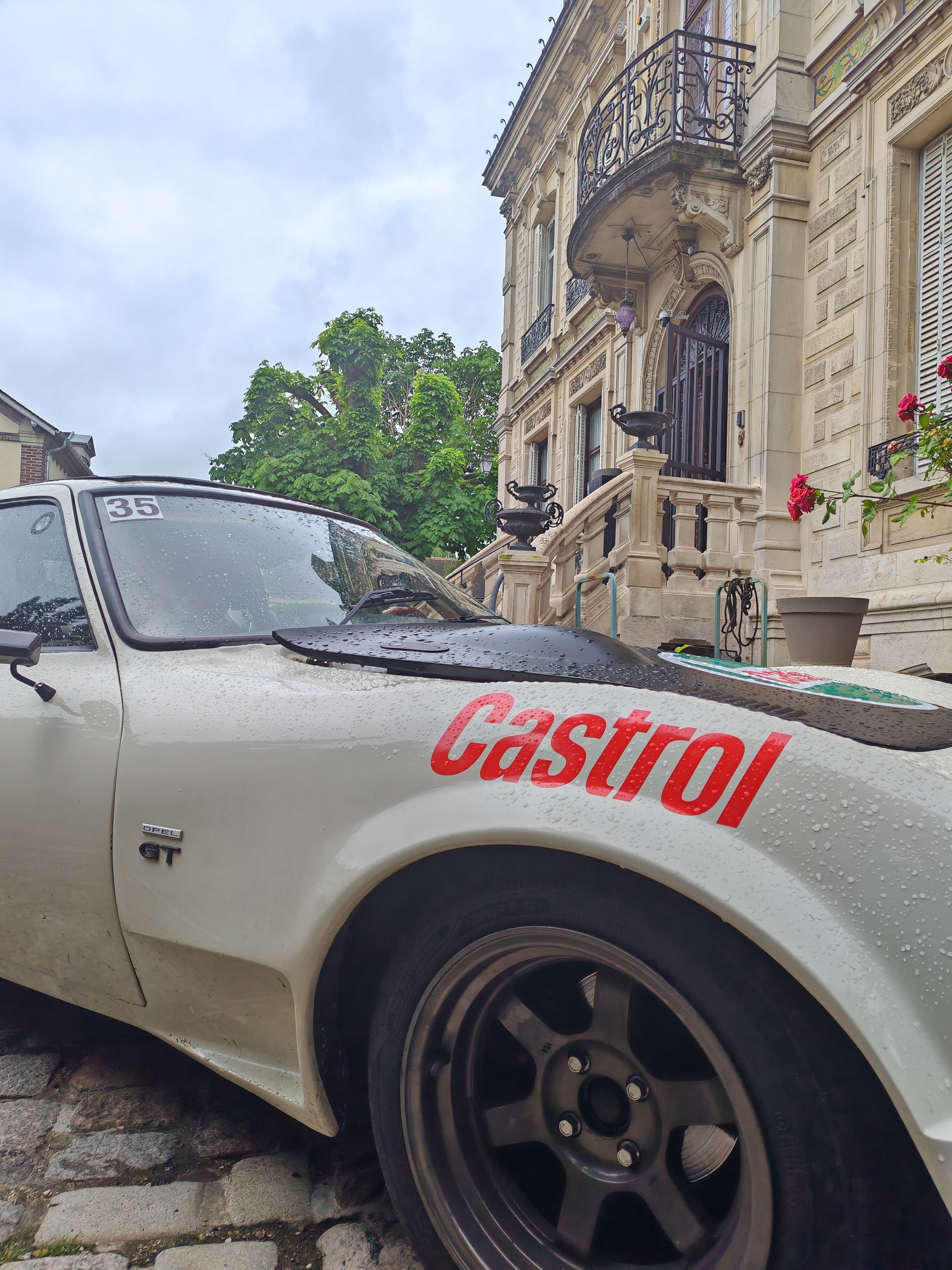 A white car with "Castrol" written on its side parked in front of a building with ornate architecture.