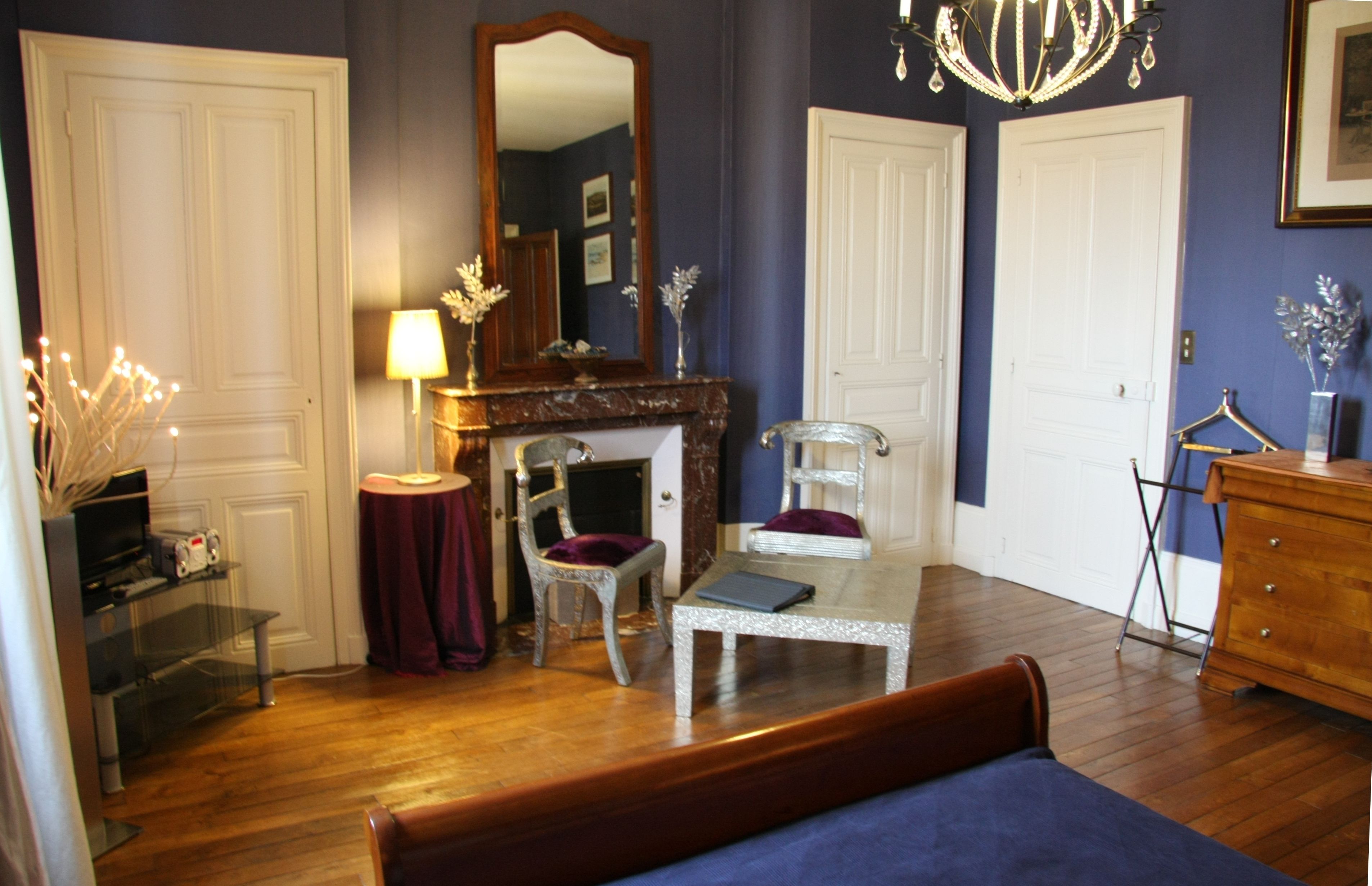 A room with a bed, a fireplace, a mirror, a chandelier, and a dresser.
