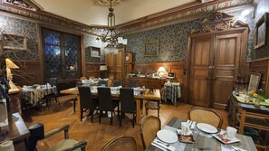 A dining area with wooden furniture, a chandelier, and patterned wallpaper. - Villa Primerose (Arcis-sur-Aube)