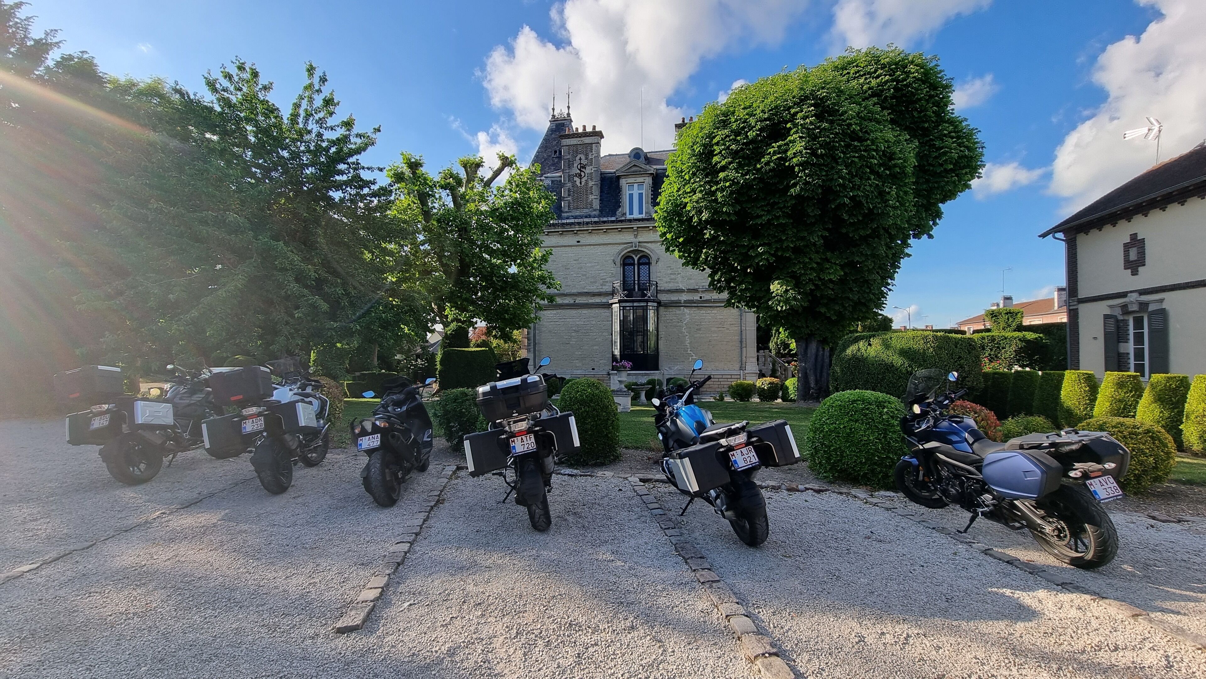 A gravel driveway with several motorcycles parked in front of a historic building with a turret and a large tree.
