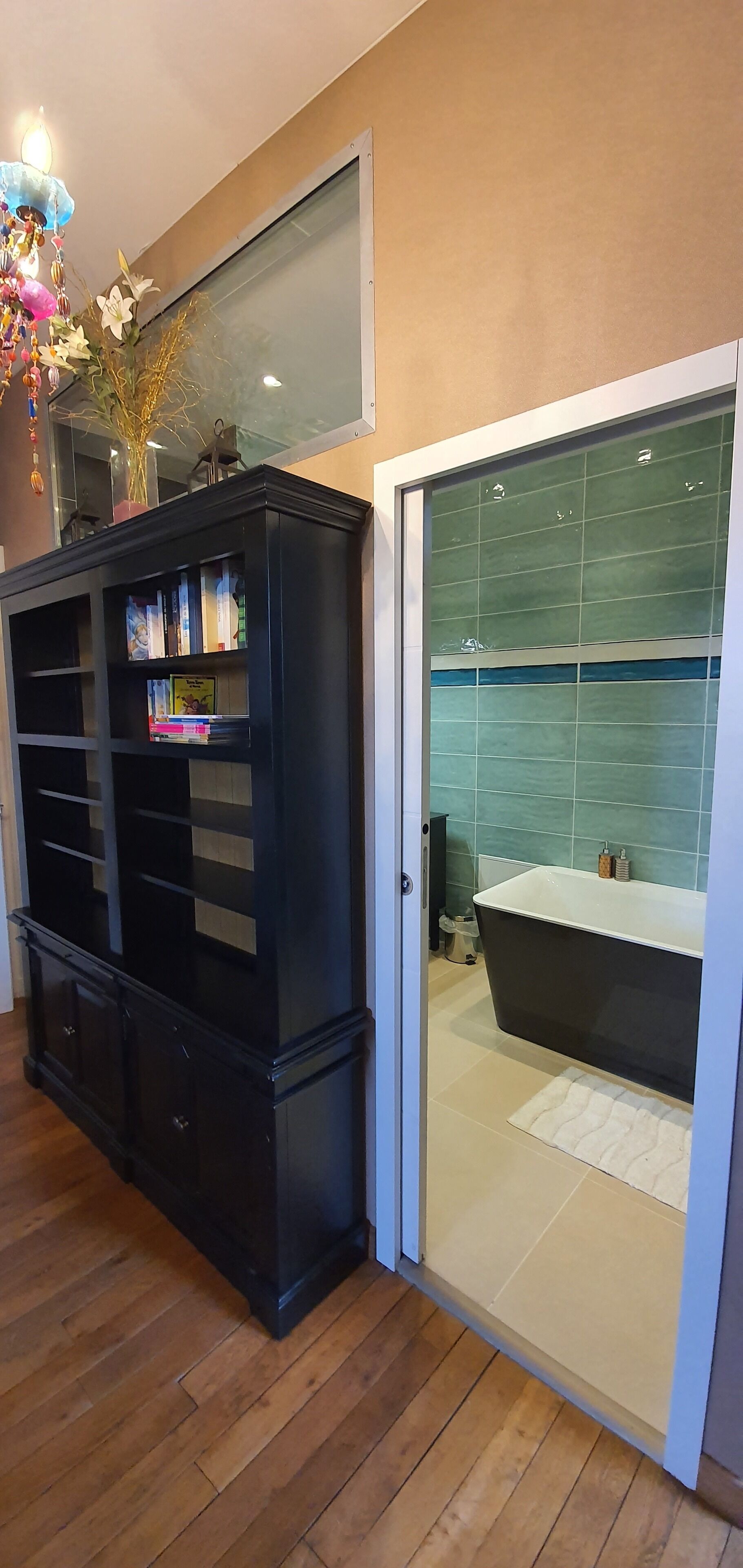 A modern bathroom with a glass-enclosed shower, a black cabinet with books, and a wooden floor.